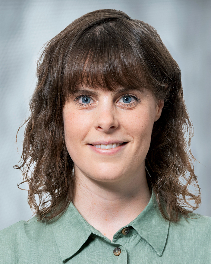 Portrait Karena Weduwen, weiblich lesbare, weisse Person mit schulterlangem, lockigem Haar und hellgrü-nem Oberteil