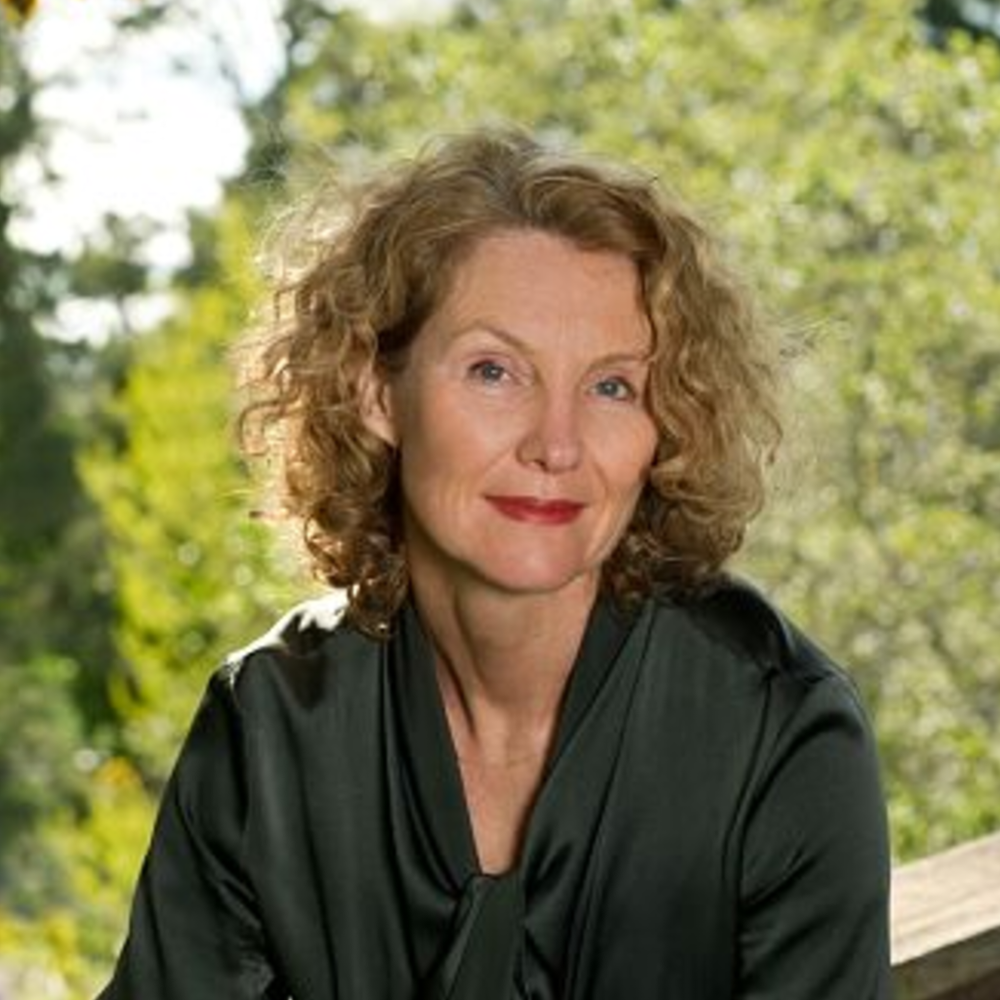 Portrait Susanna Elm, weiblich lesbare, weisse Person mit mittellangem, blondem, lockigem Haar und grüner Bluse