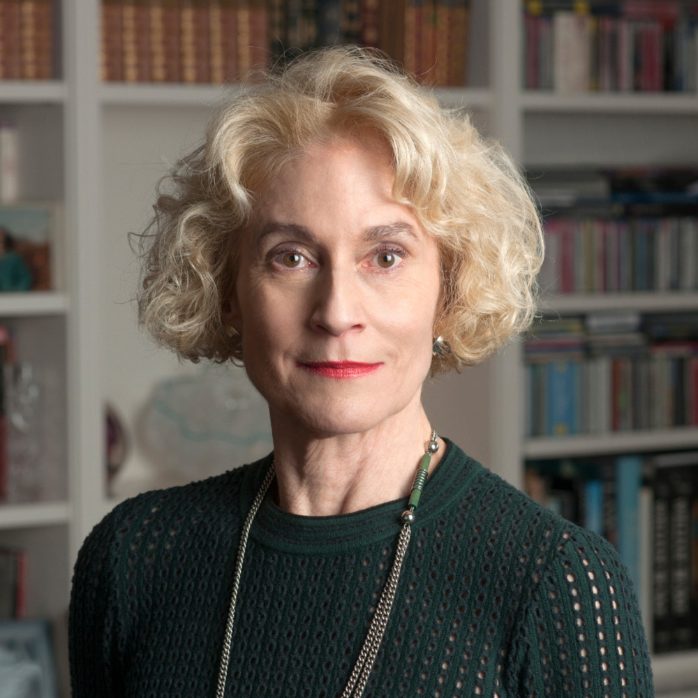 Portrait Martha C. Nussbaum, weiblich lesbare, weisse Person mit kurzen, blonden, lockigen Haaren, Ohrrin-gen, Kette und grünem Pullover