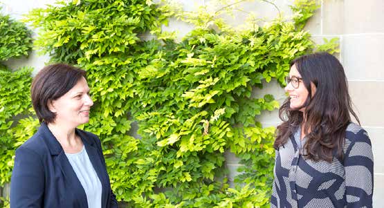 Dr. Mihaela Falub und Sibylle Hodel stehen vor einer Efeu-bewachsenen Wand und lächeln sich an.