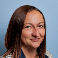 Portrait von Caroline Flammer, weiblich lesbare Person mit schulterlangen Haaren, blauem Hemd und gestreiftem Blazer