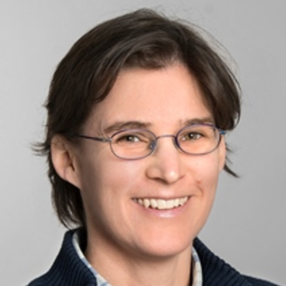 Portrait Inga Hege, weiblich lesbare, weisse Person mit kurzen, braunen Haaren, Brille, blau-karriertem Hemd und blauer Strickjacke