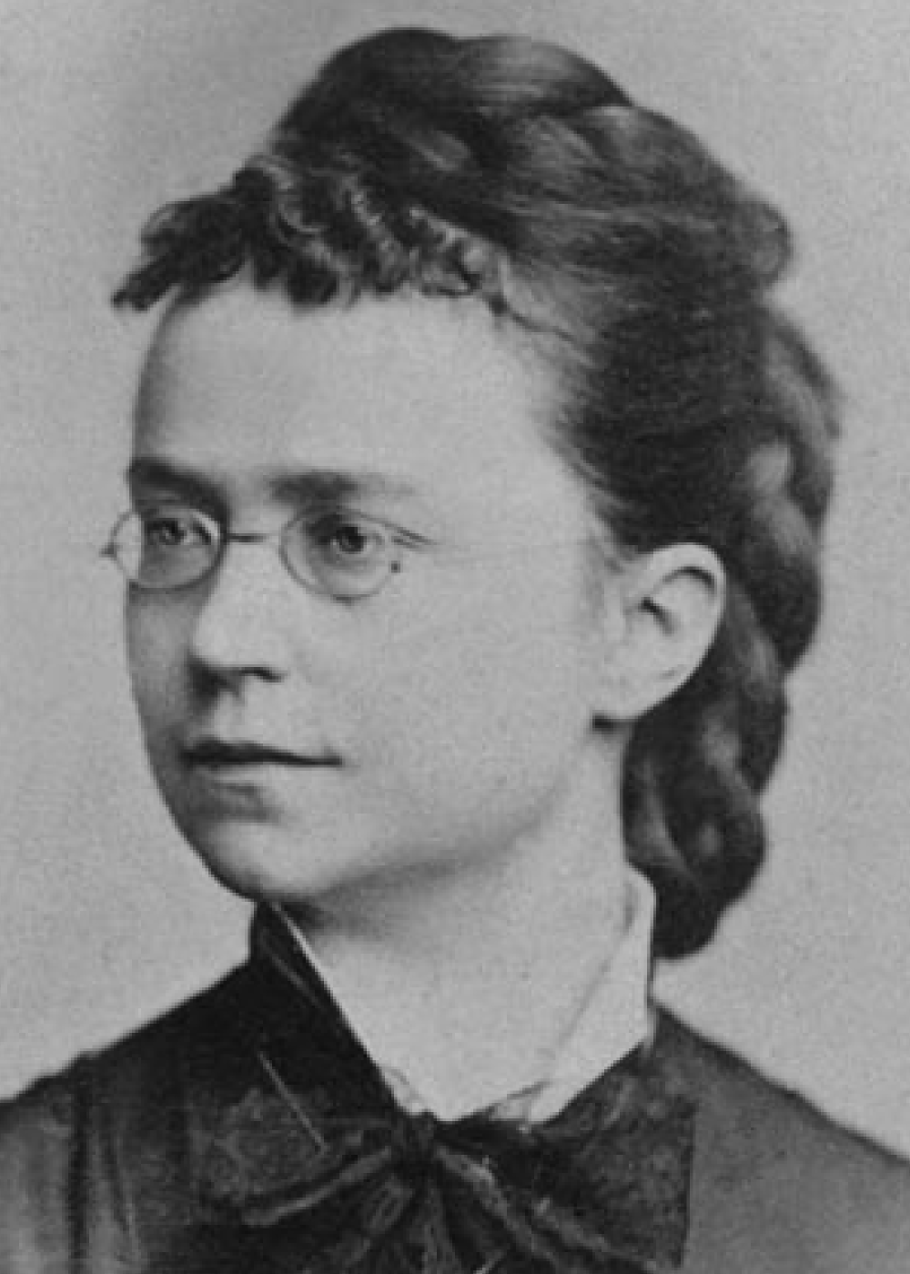 Portrait von Lydia Sesemann, Frau schaut seitlich rechts an der Kamera vorbei, sodass sie fast im Profil zu sehen ist. Die Haare sind geflochten und zu einem Zopf zusammengebunden. Sie trägt eine Brille und typische Kleidung des Neunzehntenjahrhunderts.